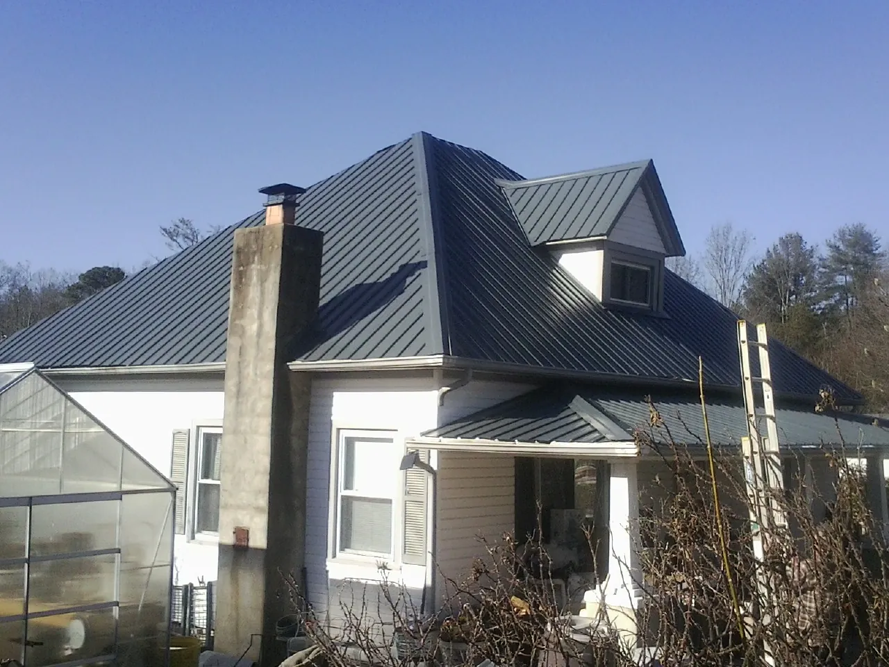 Dark blue standing seam metal roof on a white farmhouse with dormer — Slate & Tile Roof Repair by Roofing Brothers in Cabazon