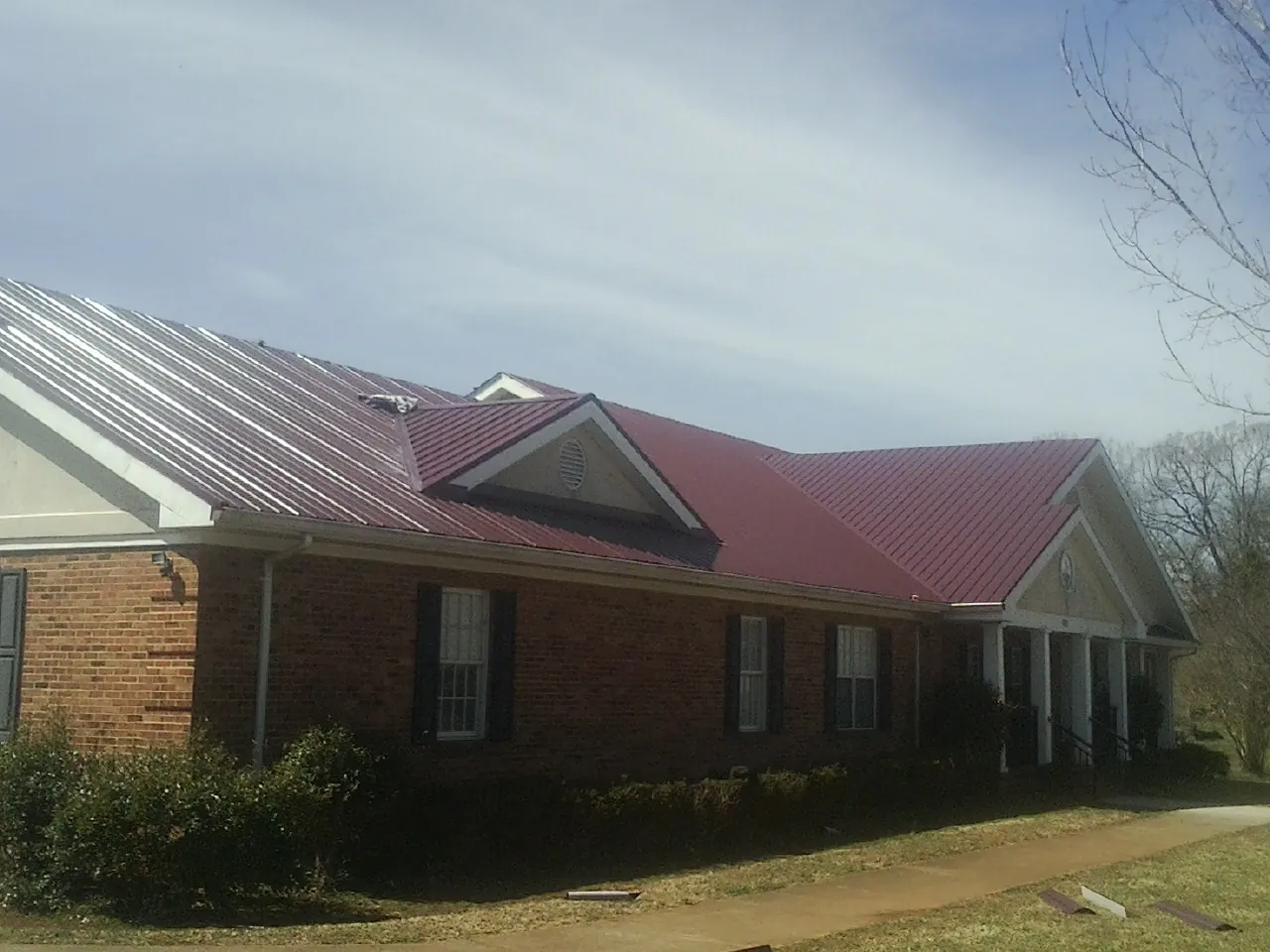Red metal roof with gabled entries on a long brick building, from a Hail Damage Roof Repair job in Cabazon